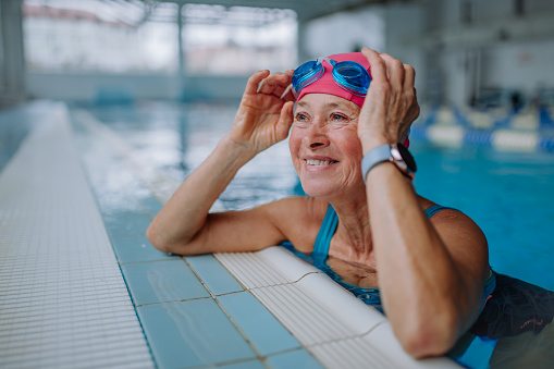 Feliz mujer mayor en la piscina, apoyada en el borde. photo