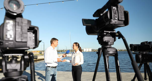 jornalista profissional entrevista jovem perto do rio em dia ensolarado - photographer camera tripod paparazzi photographer - fotografias e filmes do acervo