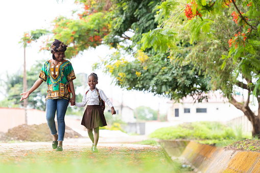 Front view mother asking schoolgirl about first day back at school walking down the road together