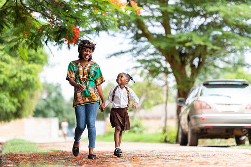 Happy mother and schoolgirl walking down rural road to school