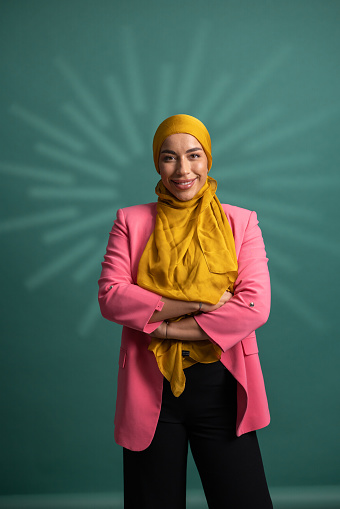 Well dressed businesswoman wearing hijab while standing in front of green background