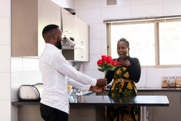 il giovane dà fiori eccitati alla moglie in cucina - men african descent giving flower foto e immagini stock