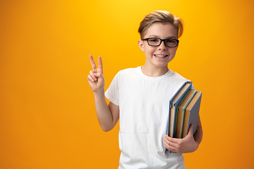 Little schoolboy holding a book against yellow background, close up