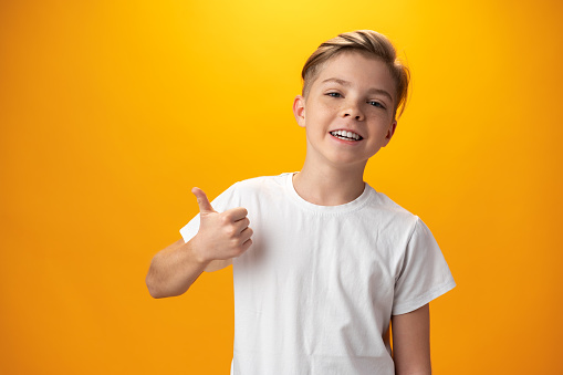 Portrait of beautiful little boy giving you thumbs up over yellow background, close up