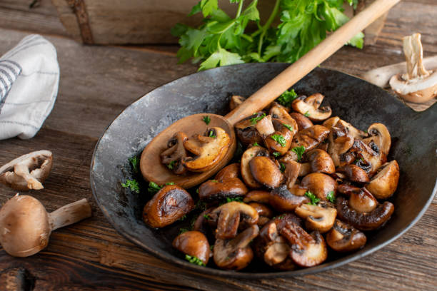 Pan fried mushrooms Delicious side dish or snack with pan fried mushrooms, champignons cooked with butter, herbs, pepper and salt. Served in a rustic cast iron pan on wooden table. mushroom stock pictures, royalty-free photos & images