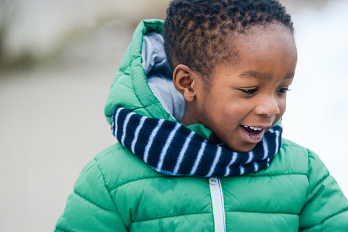 portrait of smiling african american kid in winter fashion outfit with wool scarf \noutdoors in the cold