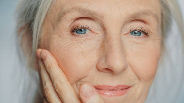 Close-up Portrait of Beautiful Senior Woman Gently Applying Face Cream. Elderly Lady Makes Her Skin Soft, Smooth, Wrinkle Free with Natural anti-aging Cosmetics. Product for Beauty Skincare retrato en primer plano de una hermosa mujer mayor que se aplica suavemente crema facial. la anciana hace que su piel sea suave, suave y libre de arrugas con cosméticos naturales antienvejecimiento. producto para el cuidado de la piel de belleza