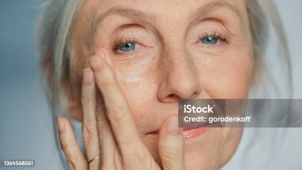 Portrait Of Beautiful Senior Woman Gently Applying Under Eye Face Cream Elderly Lady Makes Her Skin Soft Smooth Wrinkle Free With Natural Antiaging Cosmetics Product For Beauty Skincare Makeup Stock Photo - Download Image Now