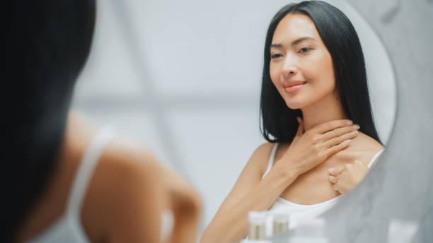 Beautiful Asian Woman Touches Her Perfect Soft Shoulder, Neck, Sensually Smiles in the Mirror. Happy Female Enjoying Her Beauty. Wellness Natural Cosmetic Skincare Products. Beautiful Asian Woman Touches Her Perfect Soft Shoulder, Neck, Sensually Smiles in the Mirror. Happy Female Enjoying Her Beauty. Wellness Natural Cosmetic Skincare Products. neck stock pictures, royalty-free photos & images