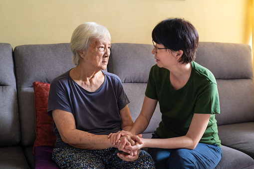 Mature Asian woman spending quality time with her depressed elderly mother at home