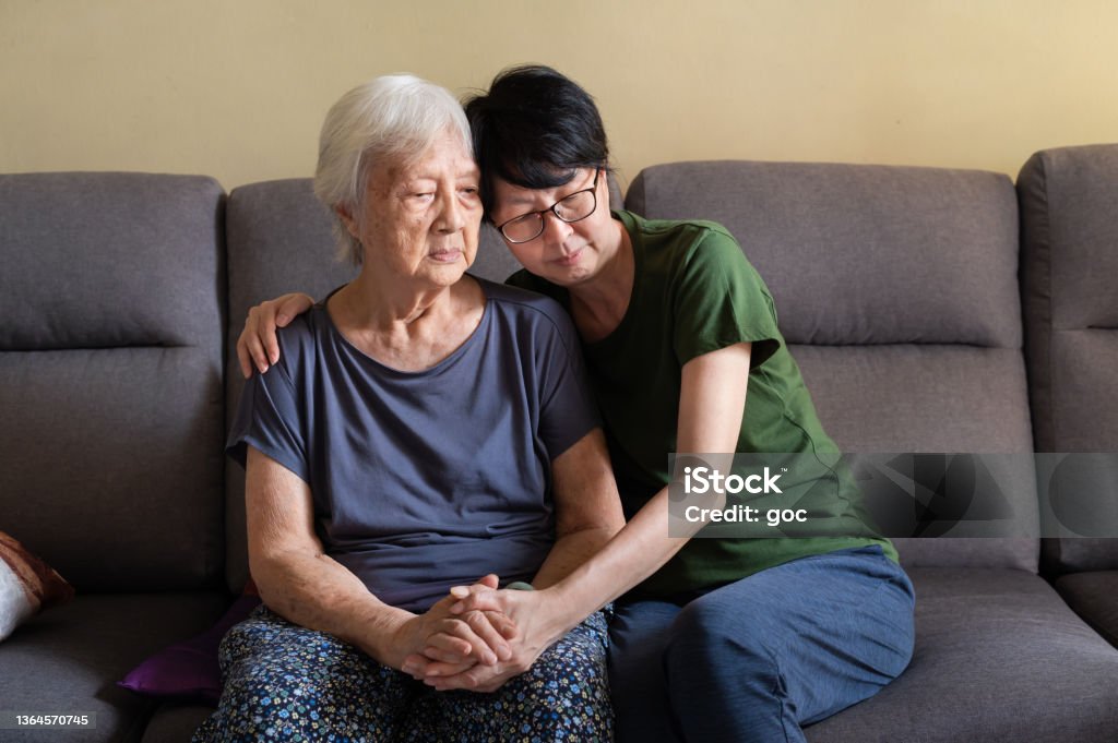 Asian daughter spending time with her elderly mother at home Mature Asian woman spending quality time with her depressed elderly mother at home. Dementia Stock Photo