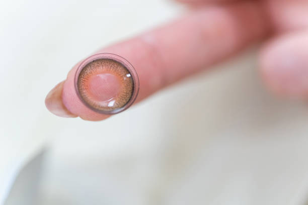 Asian woman holds a brown contact lens on her finger. stock photo