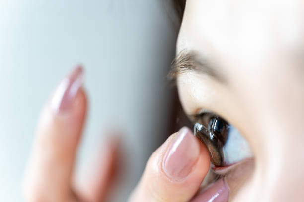 Young Asian woman inserting a contact lens in eye, brown contact lens on her finger. stock photo