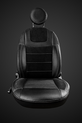 Comfortable driver car seat with round headrest in faux leather with suede inserts isolated on black background, front view