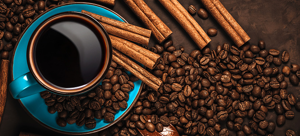 Cup of aromatic black coffee, coffee beans and cinnamon sticks on dark background. Still life. Top view. Panoramic banner.