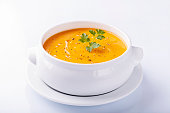 Front view of pumpkin soup on white background with olive oil and parsley