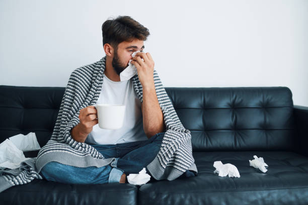 istock Sick man blowing running nose sitting on sofa at home 1364578660
