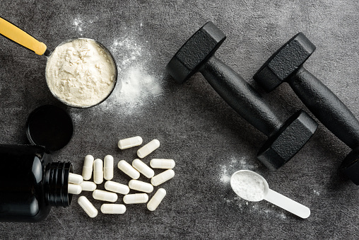 Measuring spoons with protein and creatine, BCAA capsules and dumbbells on a dark background. The concept of sports supplements.