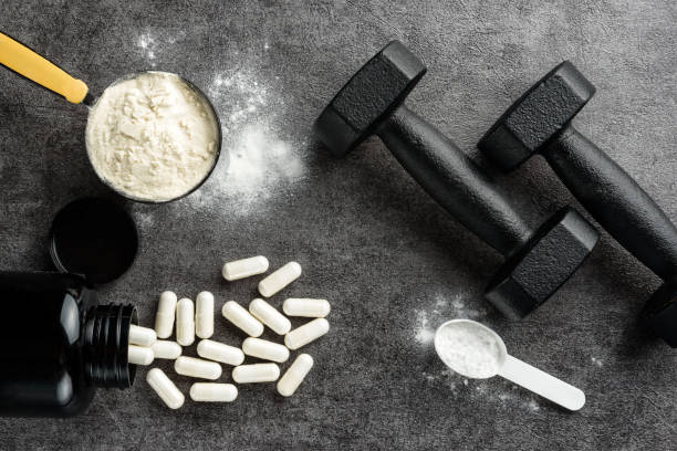 Measuring spoons with protein and creatine, BCAA capsules and dumbbells on a dark background. The concept of sports supplements. Measuring spoons with protein and creatine, BCAA capsules and dumbbells on a dark background. The concept of sports supplements. Supplements stock pictures, royalty-free photos & images