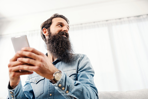 Low angle view of a bearded man holding phone and looking away.