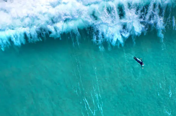 Photo of Big wave splashing behind a lonely surfer seen from above