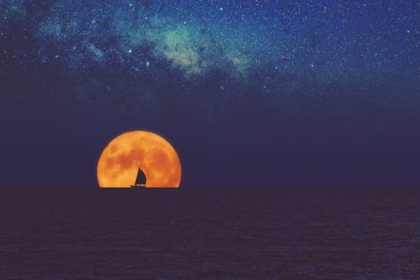満月と天の川は帆船のシルエットで海の地平線の上に上昇します。