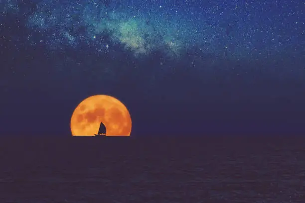 Photo of Full Moon and Milky way rising above ocean sea horizon with sailing boat silhouette.