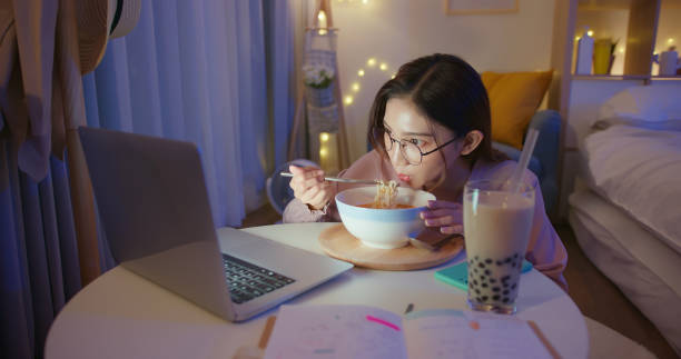 freelance woman work from home asian woman wearing eyeglasses is eating instant noodles and tapioca ball milk while working on laptop at home in the evening bubble tea photos stock pictures, royalty-free photos & images