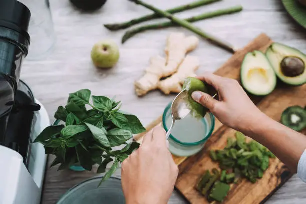 Young woman preparing detox juice with green vegetables and fruits - Focus on left hand