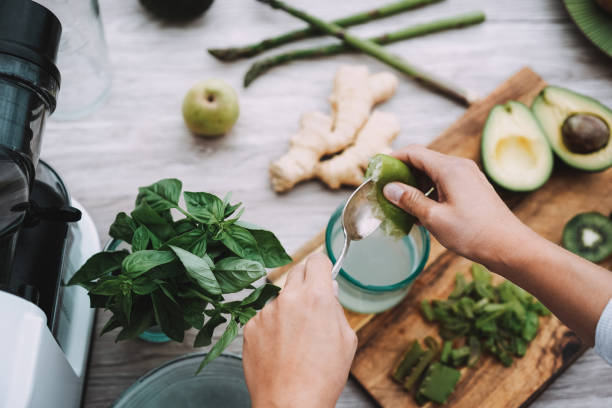 молодая женщина готовит детокс-сок с зелеными овощами и фруктами - фокус на левую руку - extracted стоковые фото и изображения