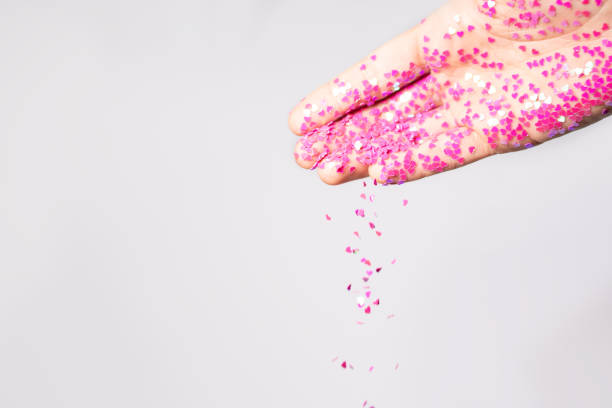 istock Small pink heart shape sequins fall from young female hand on gray background. Valentine's day concept. Female hand pour pink heart shape sequins. 1364592261