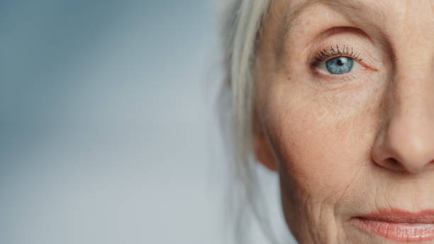 primo piano di un occhio di bella donna anziana che guarda la telecamera e sorride meravigliosamente. nonna anziana dall'aspetto splendido con bellezza naturale di capelli grigi, occhi azzurri e visione del mondo allegra - occhi azzurri foto e immagini stock