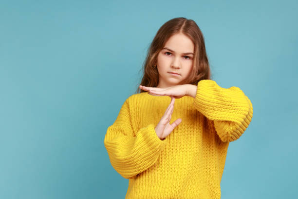 Portrait of little adorable girl showing timeout, child asking break with imploring expression. Portrait of little adorable girl showing timeout, child asking break with imploring expression, wearing yellow casual style sweater. Indoor studio shot isolated on blue background. time out signal stock pictures, royalty-free photos & images