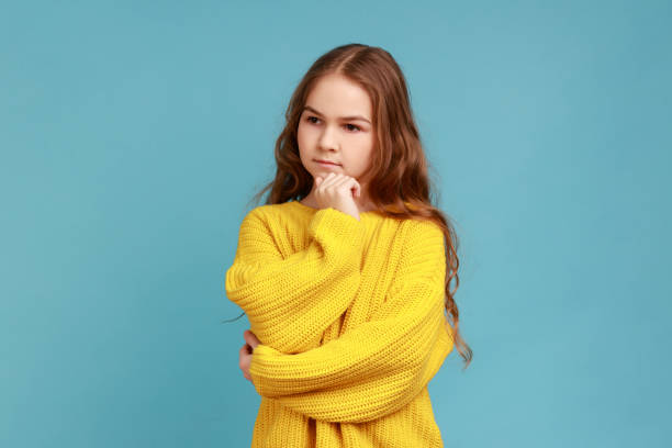 portrait of pensive little girl stands looking away with hand on chin, thinks about important things - pensive question mark teenager adversity imagens e fotografias de stock