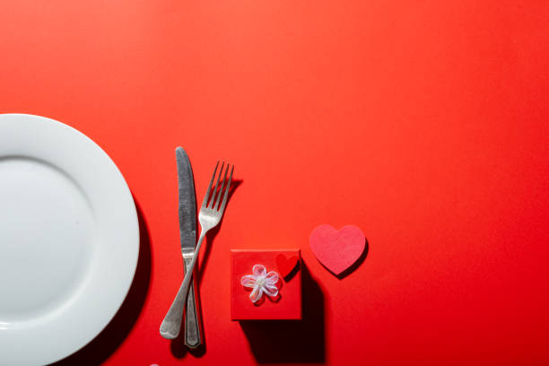 istock Empty plate with cutlery by heart shape and valentine present box on red background with copy space 1364597297
