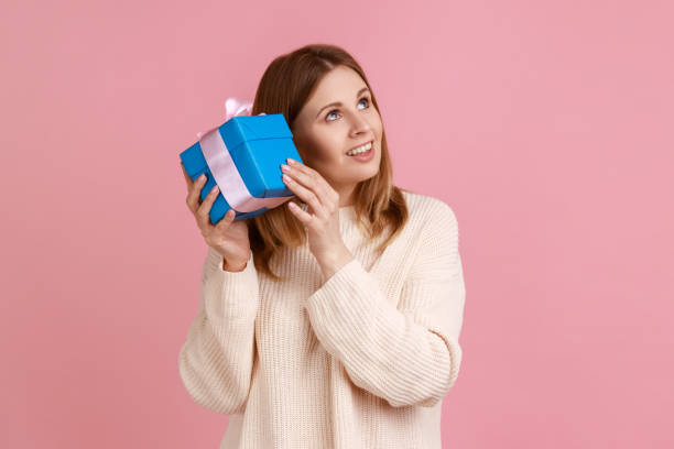 istock Curious blond woman shaking wrapped present box, being interested what inside, looking smiling away, 1364597753