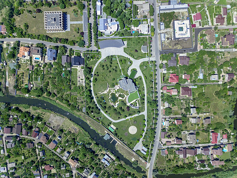 Aerial view of suburban area with private residential buildings surrounded by green lawns and gardens on banks of small river in summer day