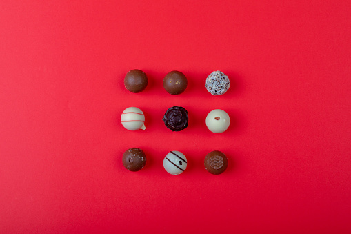 Overhead view of different chocolate spheres arranged on red background with copy space. love and valentine sweets.