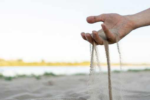 concept of time pass by, hand holding sand and pour it on the beach