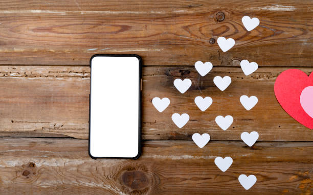istock Smartphone with blank screen showing copy space by white heart shapes on wooden table 1364604054