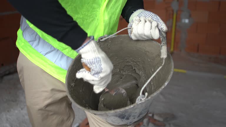 Close-up of a man construction worker mixing cement concrete in a bucket with trowel