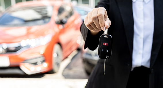 A person holding a car key, a female car rental company employee is about to deliver the car to a customer who has signed a rental contract and paid the deposit. Car rental concept.