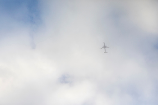 Looking up at a passenger jet obscured in a cloudy sky over London