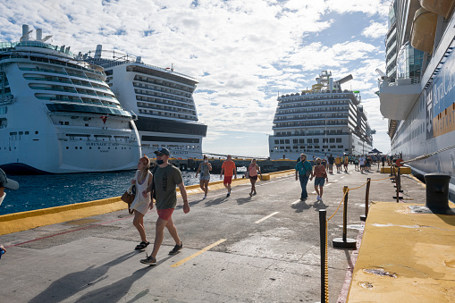 Mahahual, Mexico - January 6, 2022: Passengers, some wearing face masks, disembark from one of several cruise ships, including the Liberty of the Seas, Carnival Pride,  MSC Meraviglia, and the Serenade of the Seas, docked on Mexico's Costa Maya.