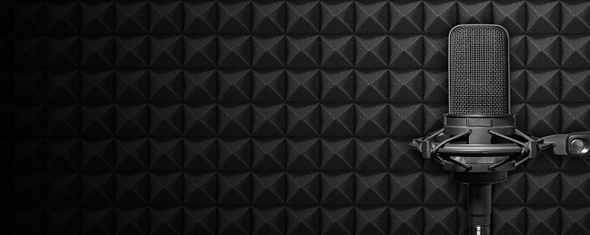 Dark podcast or recording studio background with acoustic foam and black microphone. Audio banner with copy space.