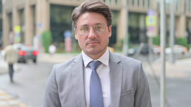 istock Middle Aged Businessman Looking at Camera while Standing in Street 1364614271