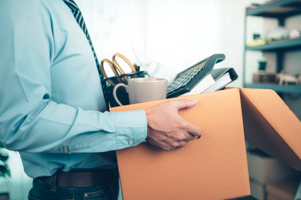 Unemployed hold cardboard box and resignation letter, dossier, alam clock, coffee cup, calculator and drawing tube in box. Quiting a job, businessman fired or leave a job concpet. stock photo