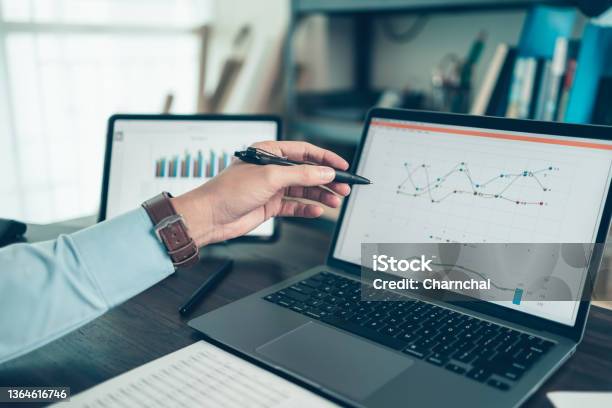 Business Man Hold Stylus Pen And Pointing To Laptop At Office With Document Report Graph Financial Report On Screen Stock Photo - Download Image Now