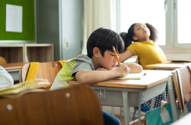 nieszczęśliwy uczeń uczący się w klasie w szkole podczas lekcji, znudzony i zniechęcony uczeń. koncepcja nawyków edukacyjnych dzieci w wieku szkolnym. - learning boredom studying child zdjęcia i obrazy z banku zdjęć