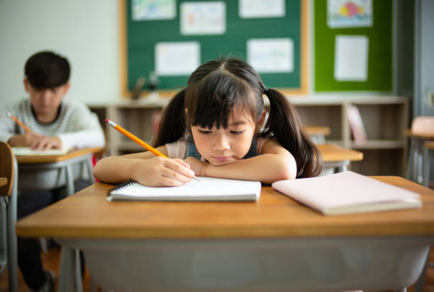 close up frustrated unhappy little schoolgirl studying in classroom at school during lesson, bored and discouraged student. school children education habit, education problem concept. - learning boredom studying child imagens e fotografias de stock